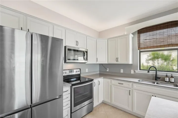 Kitchen featuring white cabinets, light tile flooring, stainless steel appliances, sink and center island