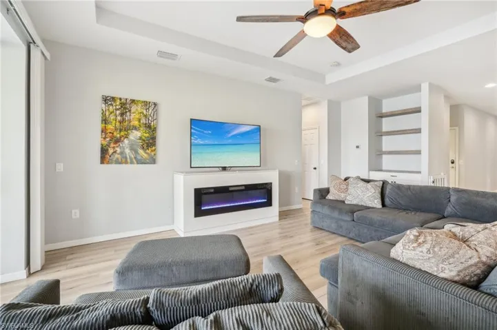 Living room with ceiling fan, electric fireplace, laminate flooring, tray ceiling, and a beautiful view of the water from the lanai