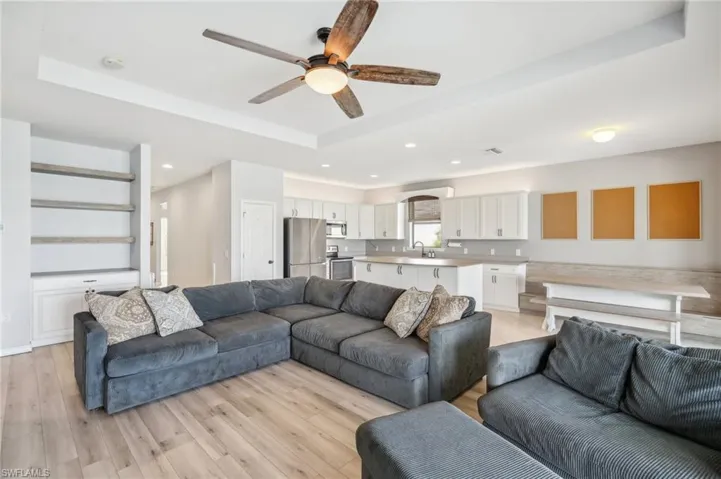 Living room with ceiling fan, electric fireplace, laminate flooring, tray ceiling, and a beautiful view of the water from the lanai