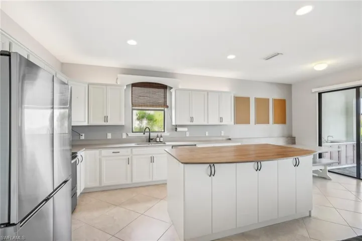 Kitchen featuring white cabinets, light tile flooring, stainless steel appliances, sink and center island