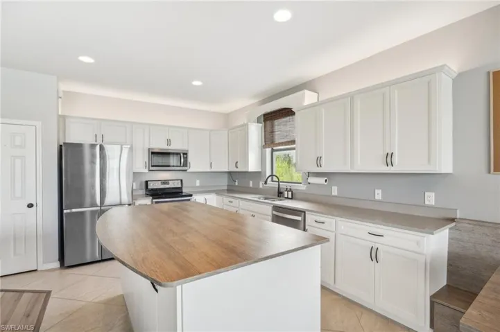 Kitchen featuring white cabinets, light tile flooring, stainless steel appliances, sink and center island
