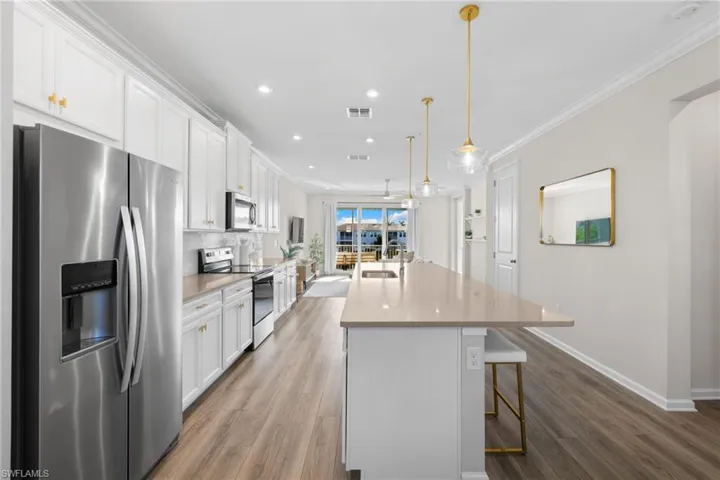 Kitchen featuring appliances with stainless steel finishes, white cabinetry, a breakfast bar, a center island with sink, and light wood-style flooring