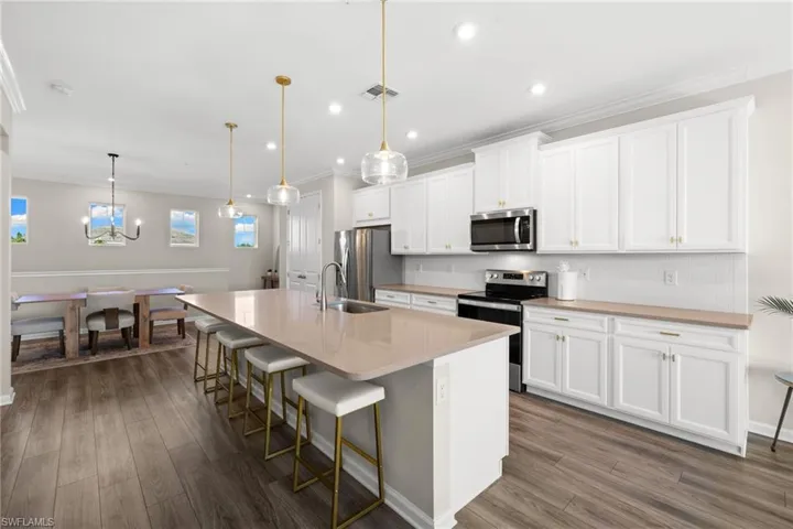 Kitchen with a breakfast bar area, stainless steel appliances, an island with sink, hanging light fixtures, and decorative backsplash