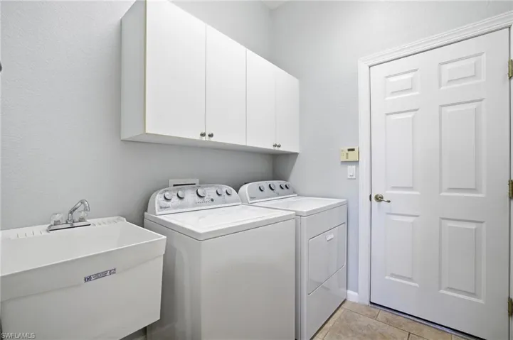 Washroom with cabinet space, washer and clothes dryer, light tile patterned flooring, and a textured wall