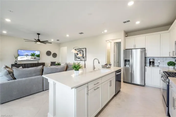 Kitchen with ceiling fan, a kitchen island with sink, white cabinets, sink, and appliances with stainless steel finishes