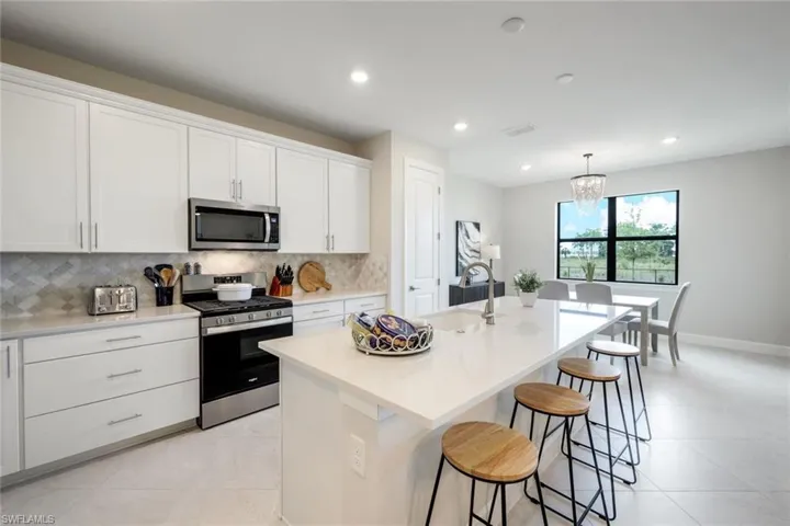 Kitchen featuring stainless steel appliances, a center island with sink, white cabinetry, light tile floors, and pendant lighting