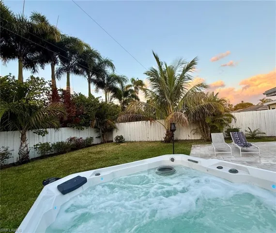 Pool at dusk with a fenced backyard and a hot tub