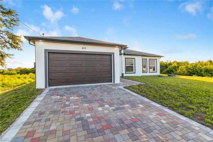 View of front of home featuring decorative driveway, a front lawn, stucco siding, and an attached garage