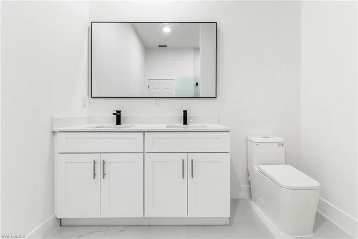 Bathroom with marble look tile flooring, toilet, baseboards, and double vanity