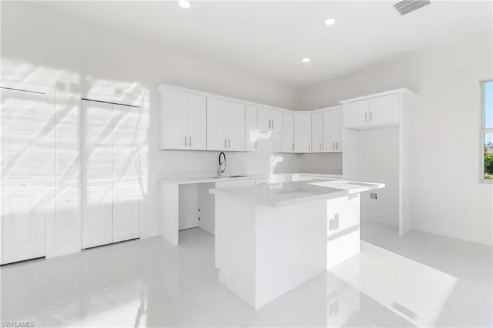Kitchen with a sink, a kitchen island, white cabinets, recessed lighting, and light countertops
