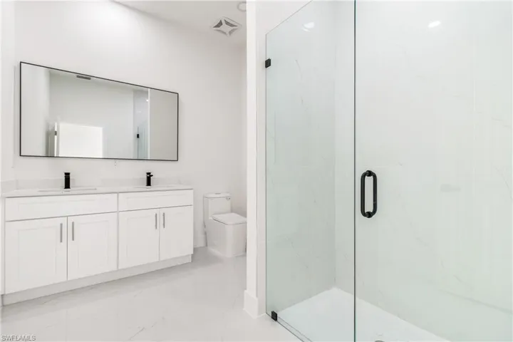 Bathroom featuring marble look tile flooring, toilet, double vanity, a marble finish shower, and baseboards