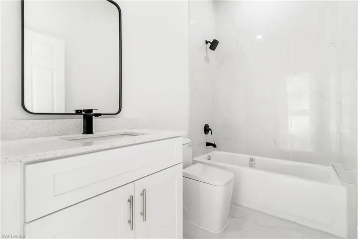 Bathroom with toilet, marble look tile flooring, vanity, and washtub / shower combination