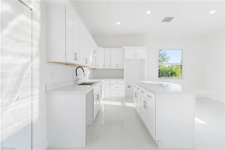 Kitchen with a sink, light marble finish flooring, recessed lighting, light countertops, and white cabinets