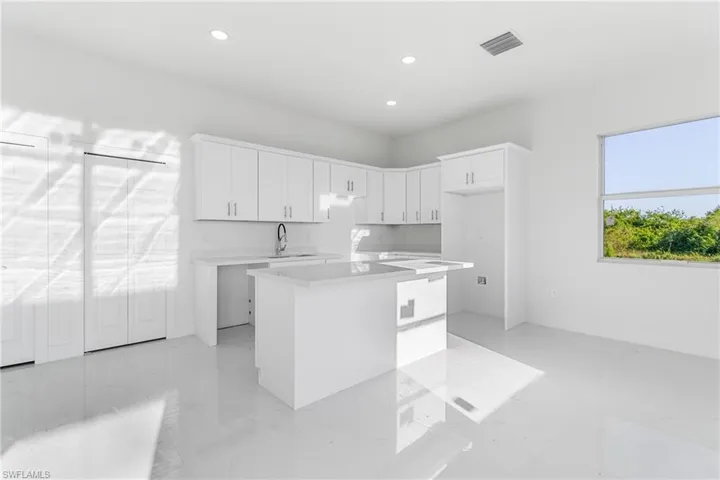 Kitchen featuring a center island, recessed lighting, white cabinets, light countertops, and a sink