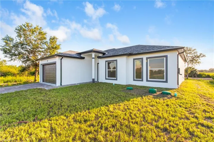 View of front facade featuring a garage, stucco siding, a front yard, and driveway