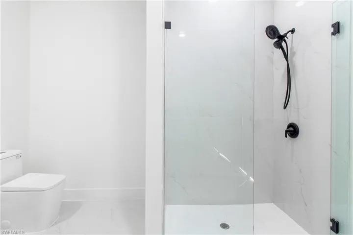 Bathroom featuring toilet, a marble finish shower, marble finish flooring, and baseboards