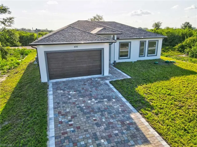 Ranch-style home featuring stucco siding, decorative driveway, a front yard, an attached garage, and roof with shingles