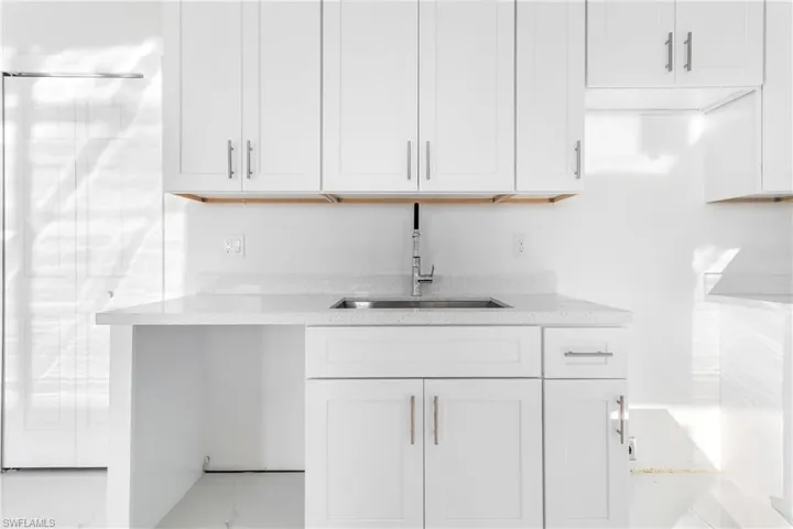 Kitchen with a sink, white cabinetry, light stone counters, and marble look tiles