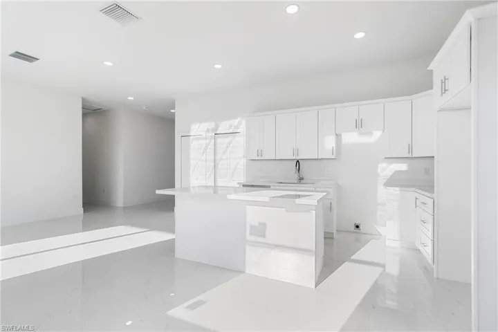 Kitchen with a sink, recessed lighting, a kitchen island, white cabinets, and light marble finish floors
