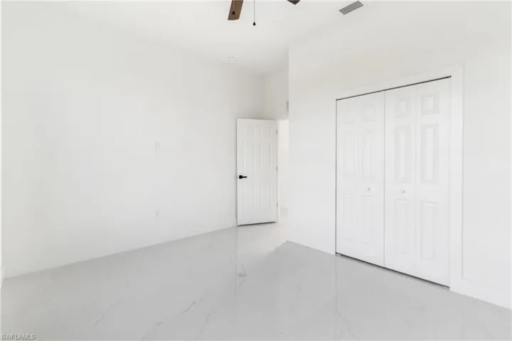 Unfurnished bedroom with light marble finish flooring, a closet, baseboards, and a ceiling fan