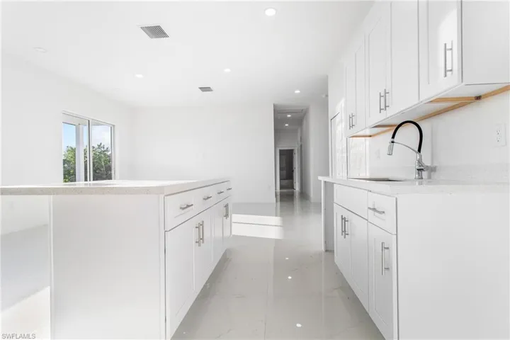 Kitchen featuring a sink, light marble finish floors, recessed lighting, white cabinetry, and a kitchen island