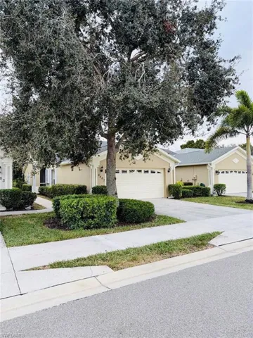 View of property hidden behind natural elements with driveway and stucco siding