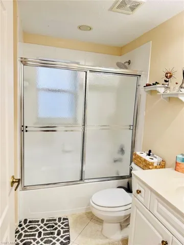 Bathroom featuring shower / bath combination with glass door, vanity, light tile patterned floors, and a textured ceiling