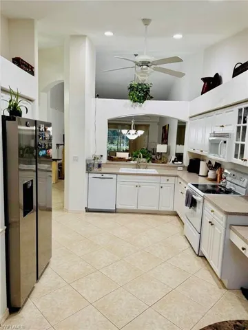 Kitchen featuring white appliances, arched walkways, high vaulted ceiling, white cabinets, and a ceiling fan