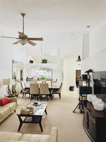 Living room with high vaulted ceiling, light colored carpet, arched walkways, ceiling fan, and recessed lighting