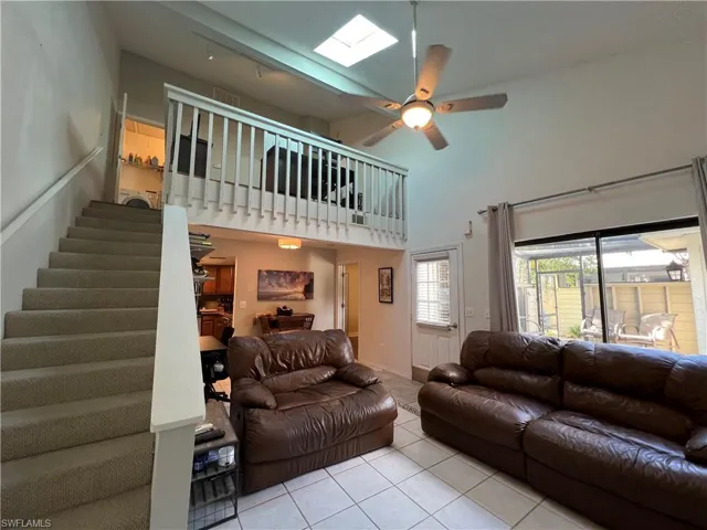Living room featuring a skylight, a towering ceiling, light tile patterned floors, and ceiling fan