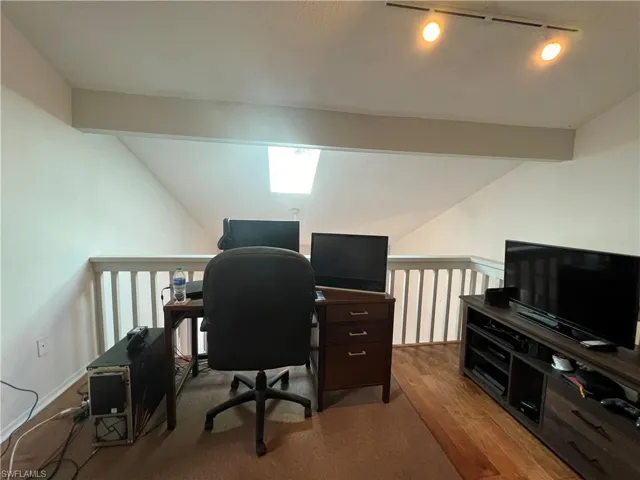 Office space with lofted ceiling with beams, light wood-type flooring, and rail lighting
