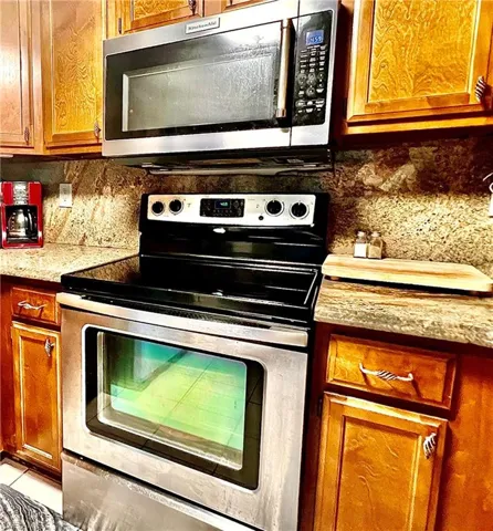 Kitchen with tasteful backsplash, light stone counters, and appliances with stainless steel finishes