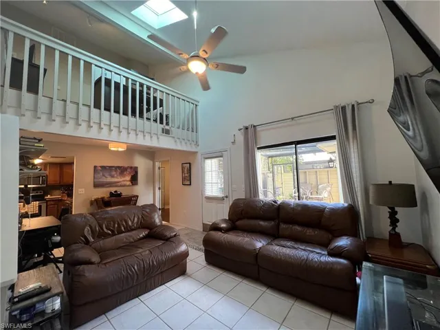Tiled living room with high vaulted ceiling, ceiling fan, and a skylight