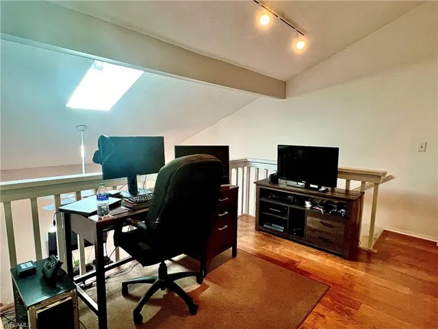 Office area with light hardwood flooring, vaulted ceiling with skylight, and rail lighting