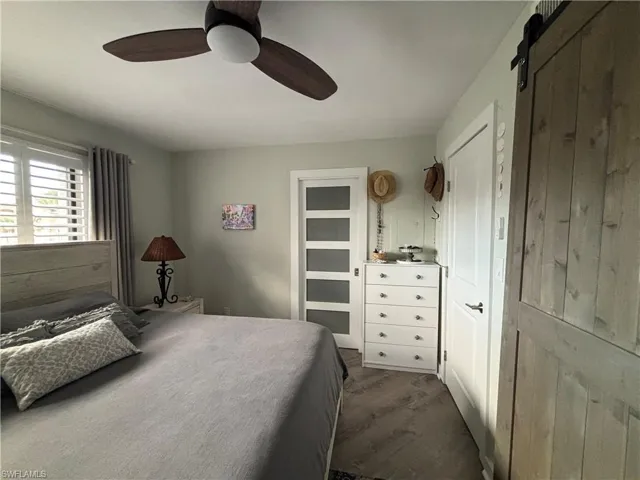 Bedroom with a barn door, dark wood-style floors, and a ceiling fan