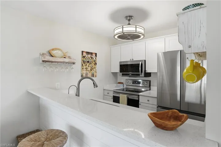 Kitchen featuring stainless steel appliances, white cabinets, light stone countertops, and a peninsula