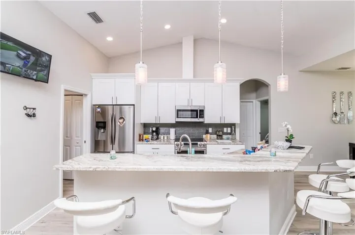 Kitchen with light wood-type flooring, appliances with stainless steel finishes, white cabinets, backsplash, and light stone counters