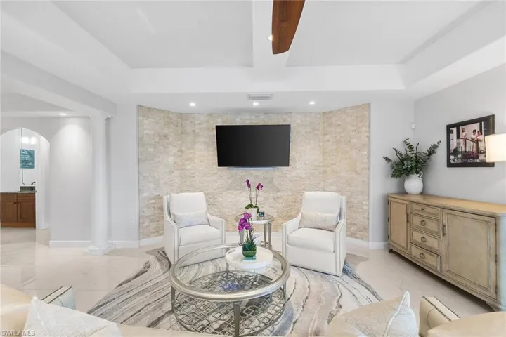 Living room with an accent wall, decorative columns, arched walkways, and beam ceiling