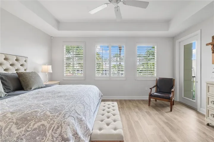 Bedroom featuring light wood-style flooring, multiple windows, a ceiling fan, and a raised ceiling