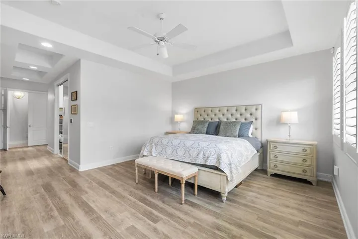 Bedroom featuring a raised ceiling, ceiling fan, light wood-style floors, and recessed lighting