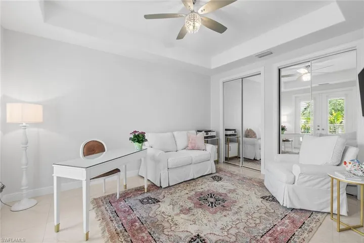 Living room featuring a tray ceiling, ceiling fan, and light tile patterned floors