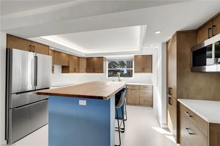 Kitchen featuring a tray ceiling, a kitchen island, stainless steel appliances, a kitchen breakfast bar, and recessed lighting