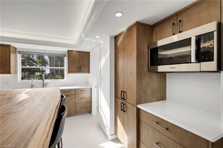 Kitchen featuring backsplash, stainless steel microwave, ornamental molding, brown cabinetry, and recessed lighting