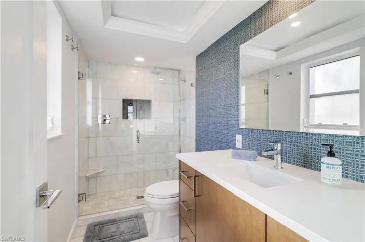 Bathroom featuring vanity, a tray ceiling, backsplash, a stall shower, and ornamental molding