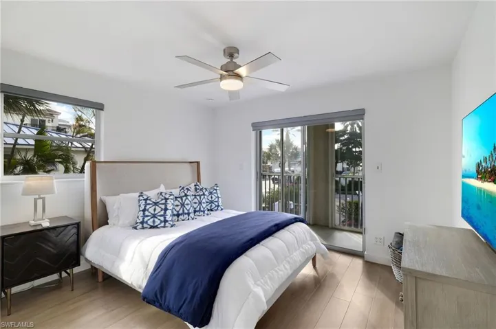 Bedroom with wood finished floors, access to exterior, a ceiling fan, and multiple windows