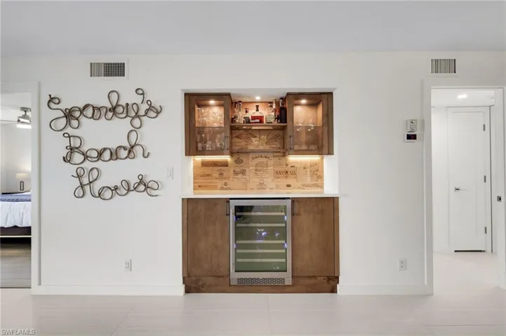 Indoor dry bar with beverage cooler, glass insert cabinets, brown cabinetry, and light tile patterned flooring