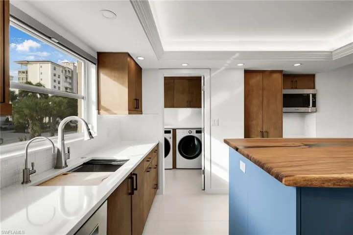 Kitchen with brown cabinets, stainless steel microwave, separate washer and dryer, recessed lighting, and light stone countertops