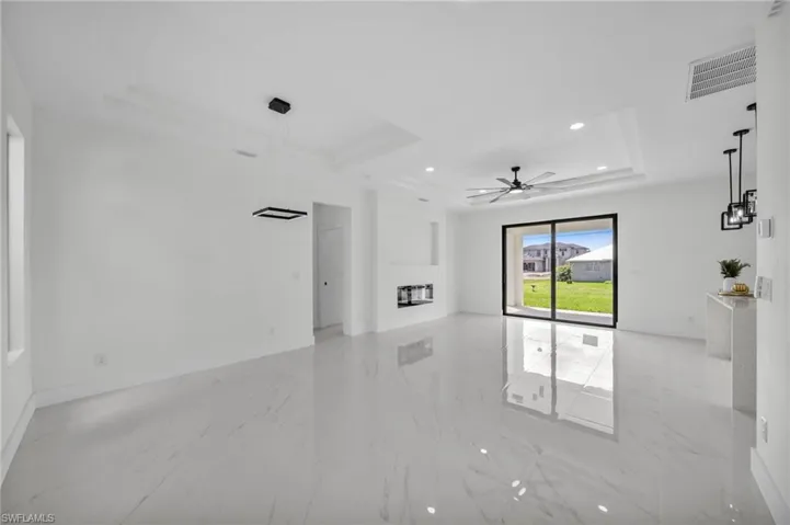 Unfurnished living room with a raised ceiling, recessed lighting, light marble finish floors, and ceiling fan