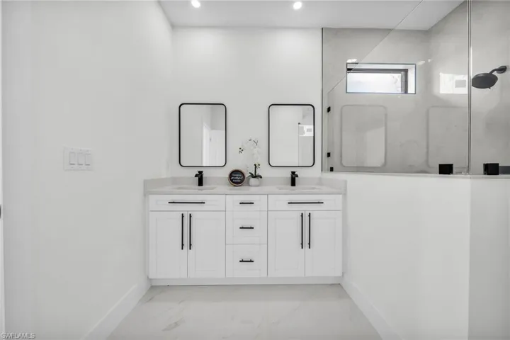 Full bath featuring light marble finish floors, a marble finish shower, and double vanity