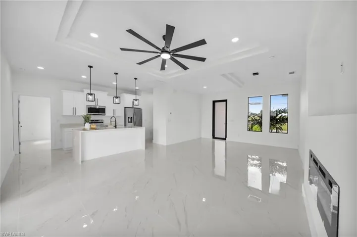 Unfurnished living room with a raised ceiling, recessed lighting, ceiling fan, and light marble finish floors